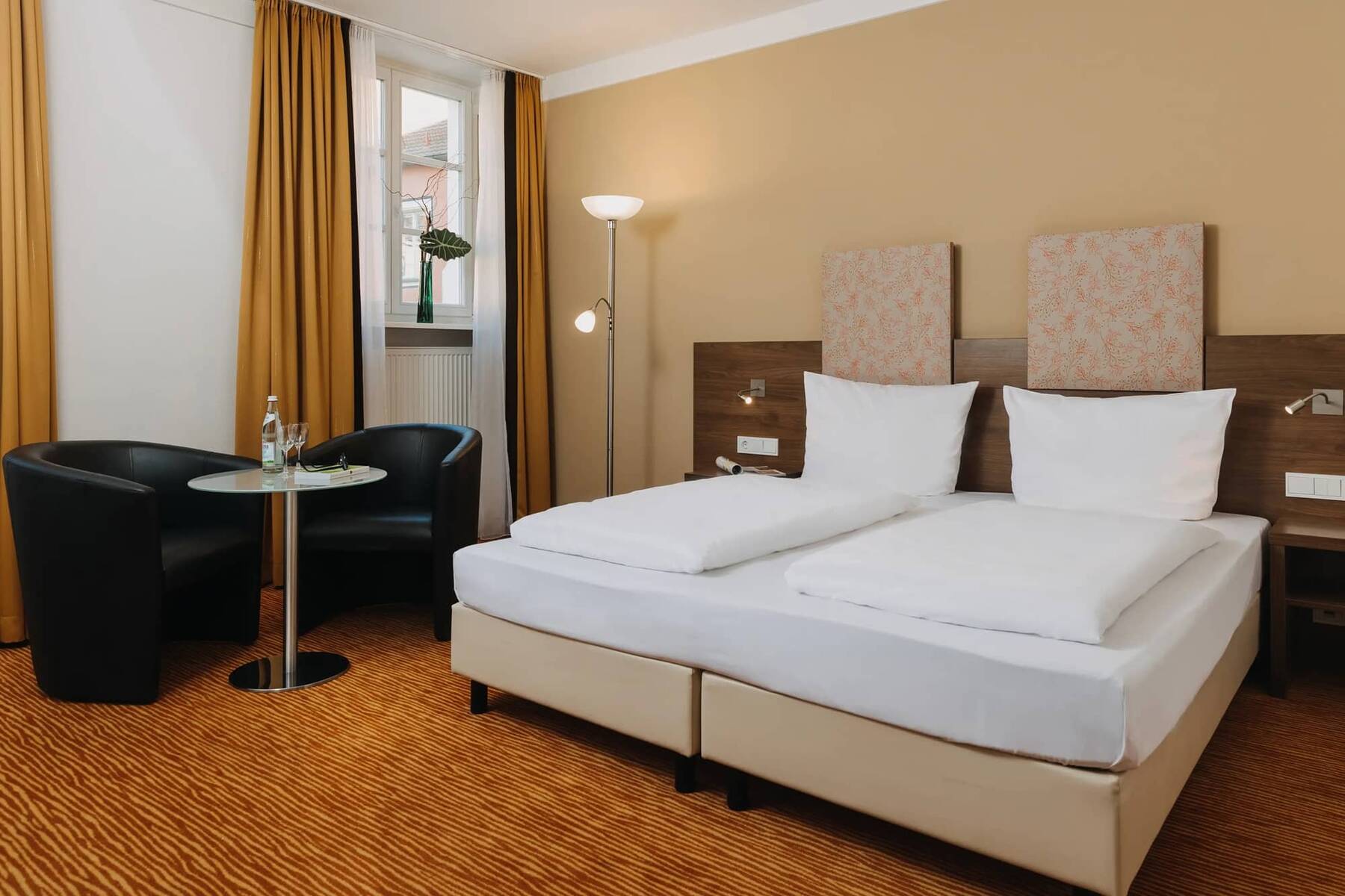 Doppelzimmer im Hotel mit zwei Betten, gemütlichen Sesseln und einem Tisch, ideal für einen entspannten Familienurlaub.