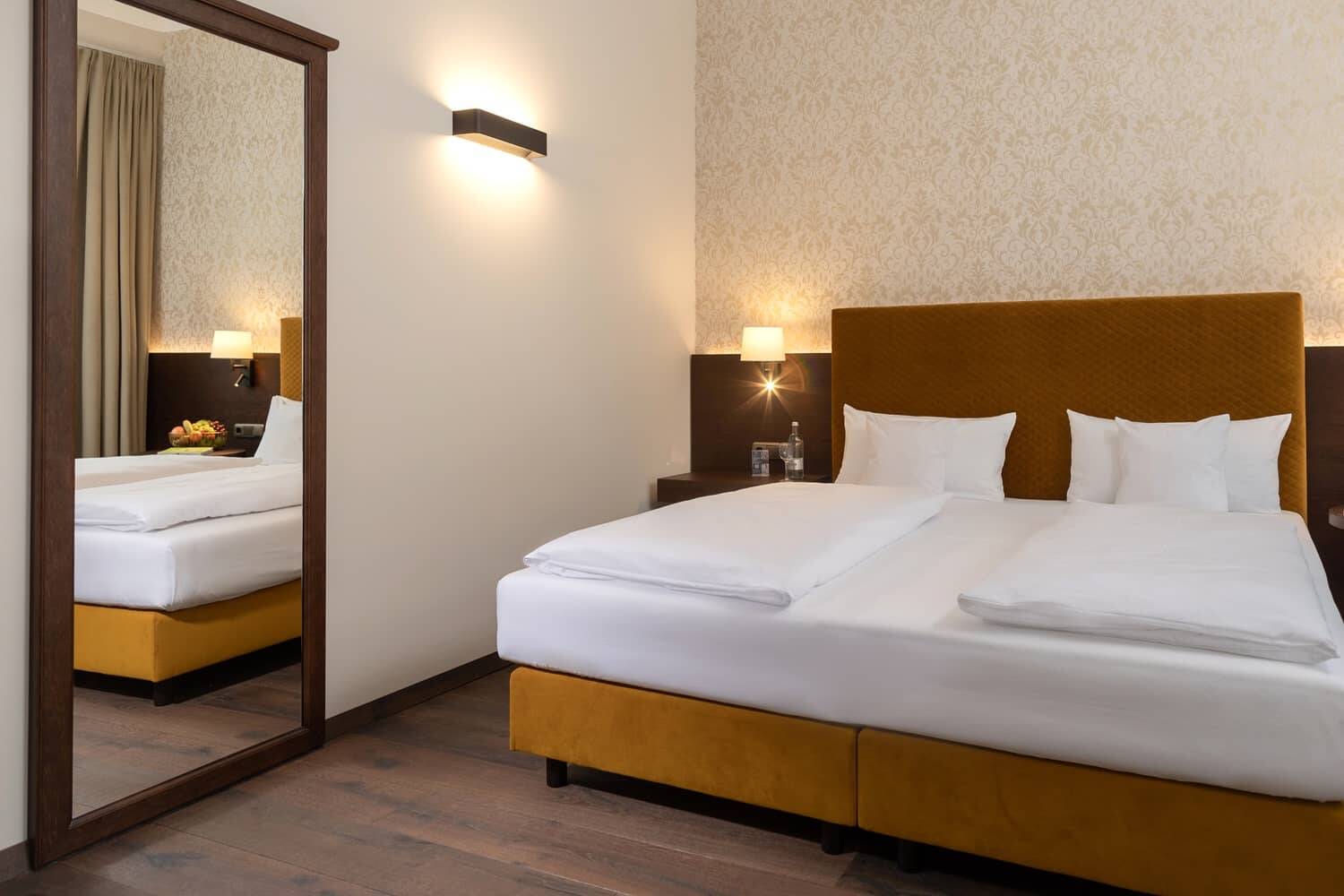 Das Schlafzimmer im Hotel Alpenglück zeigt ein modernes Bett, einen Spiegel und warme Beleuchtung, ideal für einen entspannten Familienurlaub.