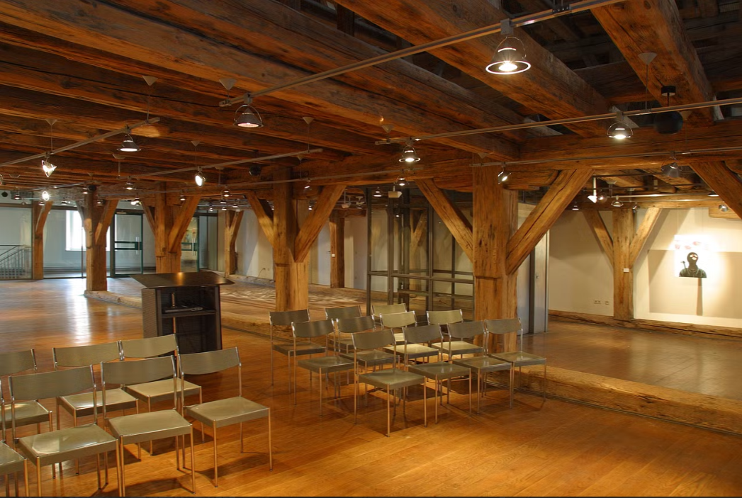 Veranstaltungsraum mit Holzdecken und -säulen, ausgestattet mit Stühlen und einem Rednerpult, ideal für Konferenzen und Events.